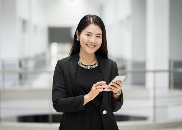 一个快乐自信的女商人穿着商务套装在办公大楼里拨打手机发短信。商业库存图片。图片下载