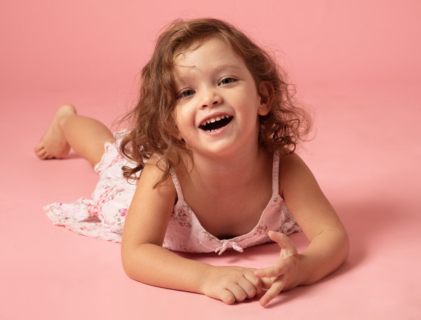 可爱的小女孩躺在粉红色的背景上。图片下载