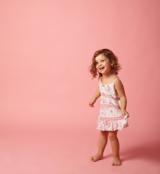 可爱的小女孩赤脚站在粉红色的背景上。图片下载
