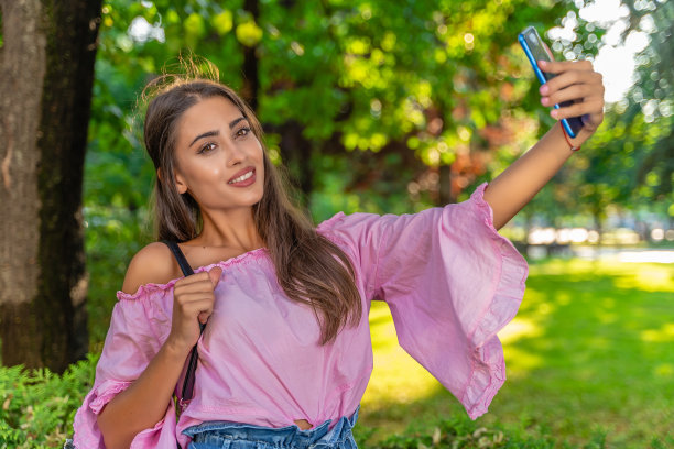 年轻美丽的女孩在公共城市公园自拍图片下载