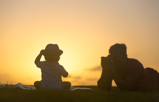 一个剪影的父亲拍照他可爱的儿子戴着一顶帽子的日落。图片下载