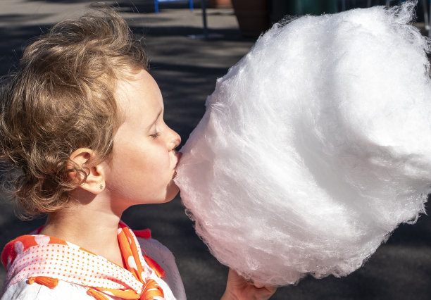 5岁白人女孩，吃棉花糖很开心。家庭周末去公园。图片下载