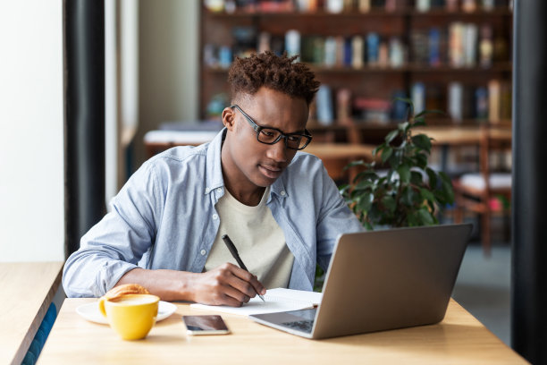 一个严肃的黑人在城市咖啡馆的笔记本电脑前边学习边做笔记图片下载