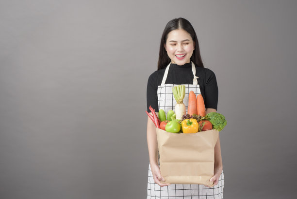 美丽的年轻女人的肖像与蔬菜杂货袋在工作室灰色的背景图片下载