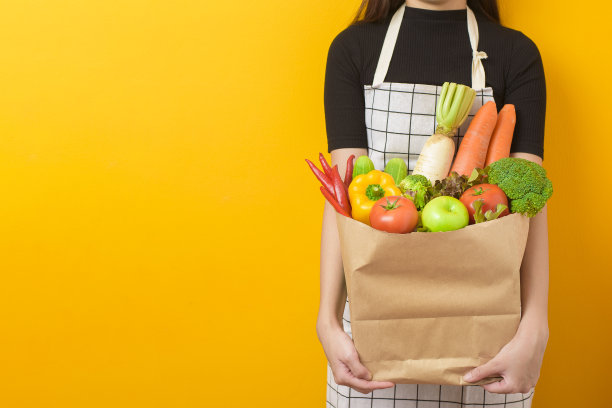 美丽的年轻女子是拿着蔬菜杂货袋在工作室黄色的背景图片下载