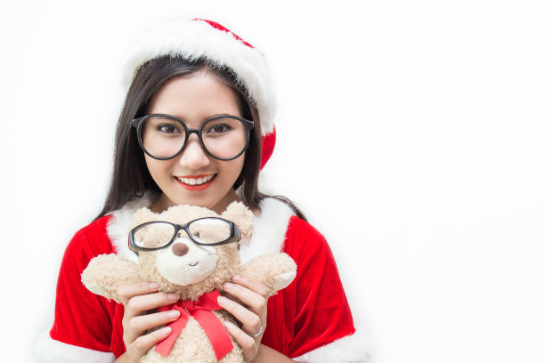亚洲美丽的女人的肖像穿着圣诞老人的服装和眼镜抱着泰迪熊。微笑快乐的亚洲女孩孤立在白色的背景。圣诞派对和假日概念图片下载