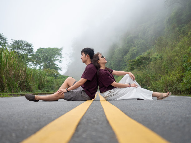 一对亚洲夫妇背靠背坐在道路中心线上。雾天山上的路。图片下载