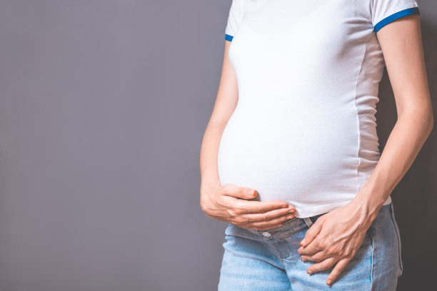 在灰色的背景下，孕妇双手放在肚子上。复制空间、怀孕、母性、人与期望的概念。特写，复印空间，室内。怀孕的照片图片下载