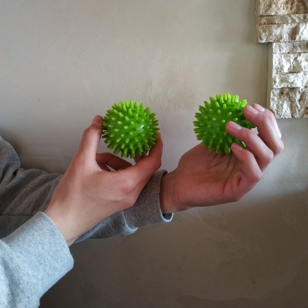 女性双手握着类似冠状细胞的绿色按摩球图片下载