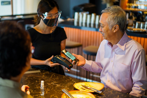 亚洲老年夫妇在餐厅用餐后进行非接触式付款。图片下载