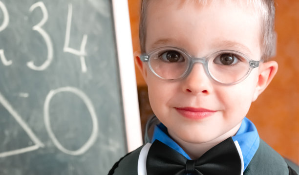 戴眼镜的可爱的小男孩站在教室里画着数字的黑板旁边。学校教育理念。素材图片
