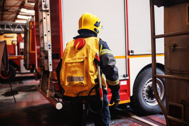 后视图勇敢的消防队员在完整的保护制服与设备站在消防站和准备行动。图片下载
