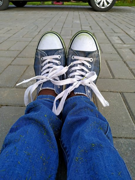 蓝色运动鞋和蓝色牛仔裤沾着新割的草在瓷砖背景上图片下载