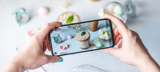 一名妇女正在用手机拍下一杯清晨的达尔戈纳咖啡。白色背景，柔和的颜色和淡紫色的花图片下载