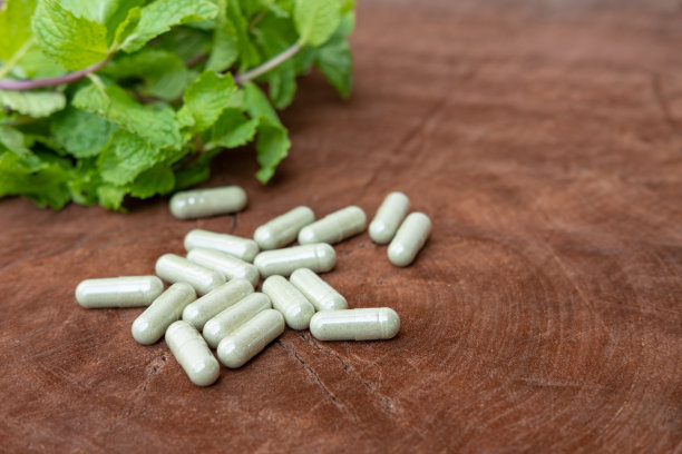 选择性聚焦于男性手持医用绿色草本胶囊与模糊的新鲜有机绿色草本叶子和胶囊在木材背景上。自然医学保健理念图片下载