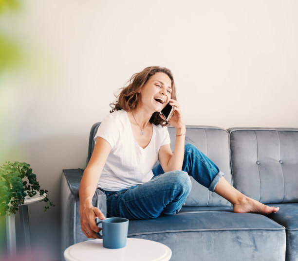 幸福随意的漂亮女人坐在家里的沙发上讲电话，喝着咖啡图片下载