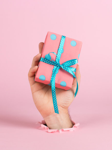 一只男性的手从粉红色背景纸上的一个洞中伸出来，手里拿着一件工艺品。圣诞概念，打印空白，复制空间。图片下载