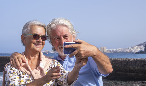 微笑的老年夫妇与白头发有乐趣的智能手机和自拍-水平线和海景-概念活跃的老年人在假期图片下载