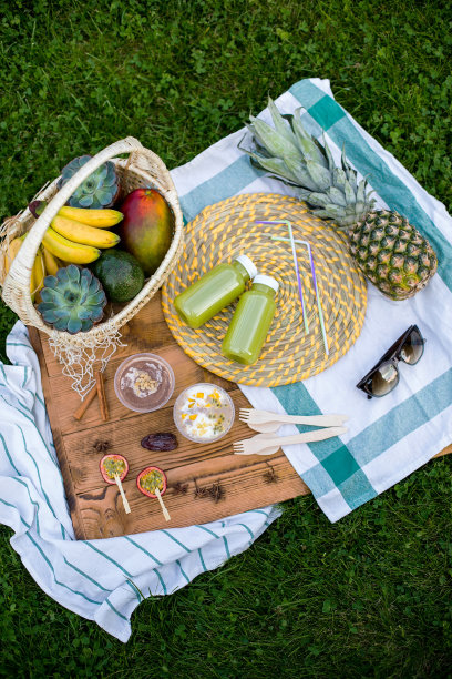 素食野餐。木制的背景是由芒果、菠萝、香蕉和箭果制成的热带水果甜点。旁边是两瓶绿色冰沙和一篮子热带水果。平躺图片下载