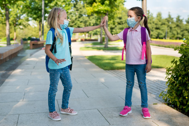 疫情隔离后学校重新开放，戴防护口罩、背书包的两个小学生在校外相遇。开学第一天概念照片图片下载