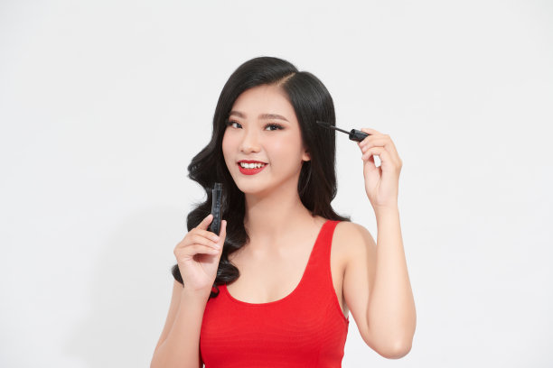 室内照片积极有吸引力的亚洲女人微笑着，而拿着睫毛膏和应用它图片下载