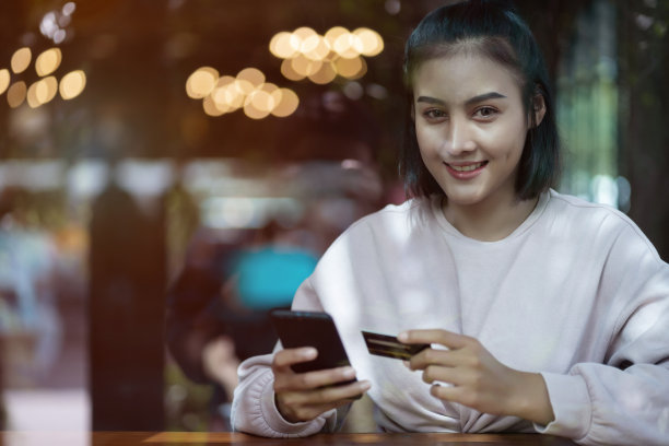 一个亚洲少女的肖像，冷静下来，并通过信用卡和智能手机支付在咖啡馆。股票的照片。图片下载