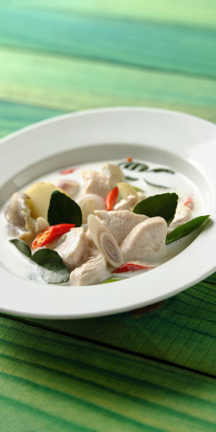 著名的国际知名泰国鸡椰奶“汤姆卡盖”，在一个碗，在绿色/绿松石色木面板的桌子背景。图片下载