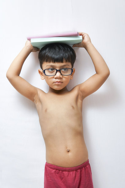 赤膊小书呆子拿着一堆书在他的头顶和站在白色的背景。图片下载