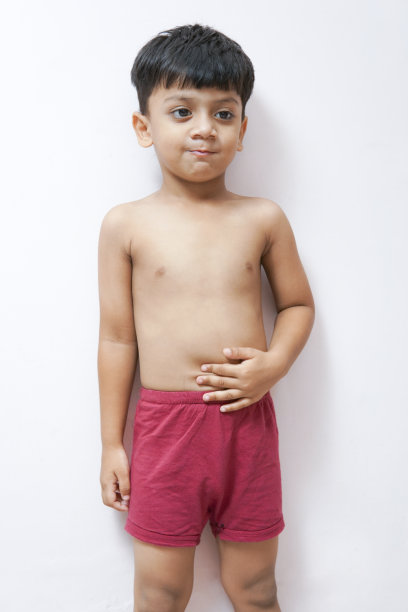 赤膊可爱的小男孩穿着红色的内衣裤，抱着肚子，站在白色的背景下。图片下载