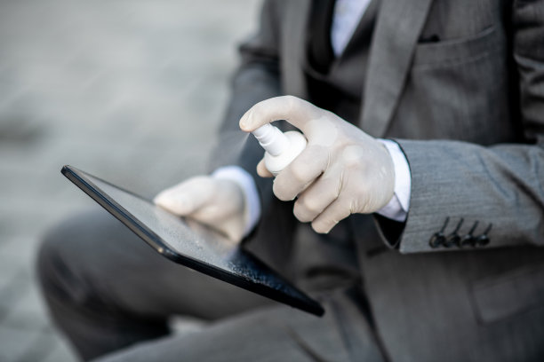 一名穿着西装的年轻人向他的笔记本喷洒消毒剂，这是病毒大流行期间的措施图片下载