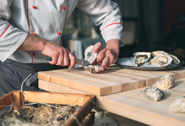 打开中空和扁平的牡蛎。厨师在餐厅里打开生蚝。图片下载