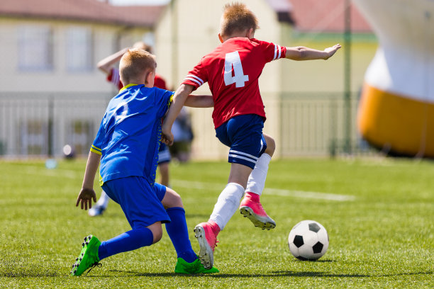 孩子们在足球场上踢球。体育足球水平背景。背景是体育场的观众。穿着红色和蓝色足球衫的青少年运动员。体育教育图片下载