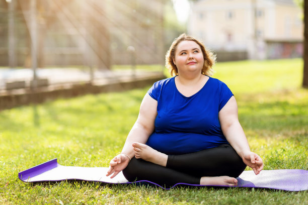 在一个阳光明媚的夏天晚上，年轻的大尺寸金发女郎在体操地毯上沉思。健康的生活方式的概念图片下载