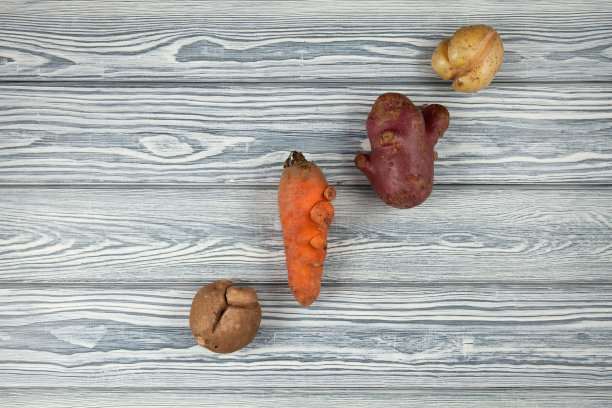 三个丑陋的土豆和一个不寻常的胡萝卜在一个带有拷贝空间的浅色木制背景上。概念-减少有机废物图片下载