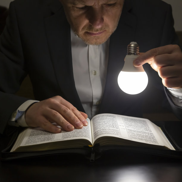 男人在LED灯的灯光下阅读圣经。寻找上帝，研究这本书。基督教和宗教图片下载