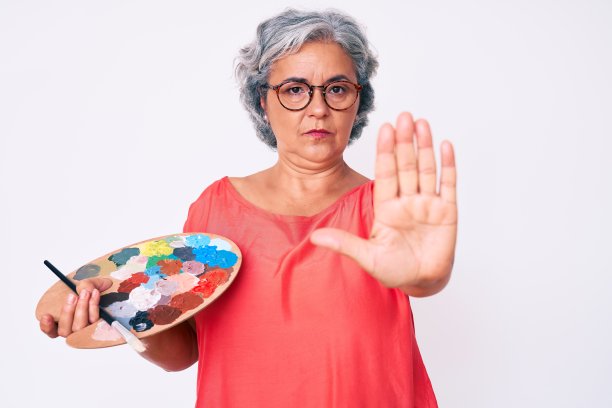 高级西班牙灰色头发的女人拿着画笔和调色板与开放的手做停止标志与严肃和自信的表情，防御手势图片下载