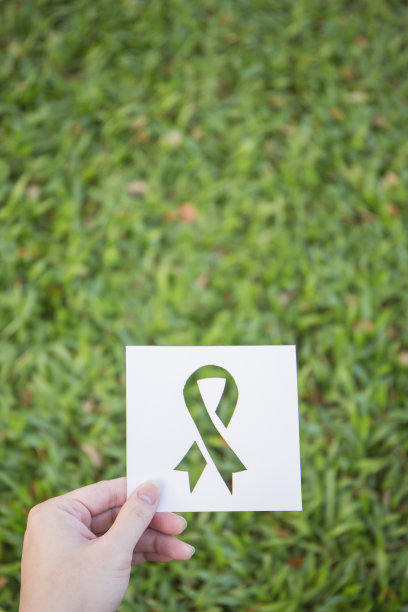 手握刻有丝带图案的剪纸，背景为绿色玻璃。乳腺癌意识的象征。保健和医疗春的概念图片下载