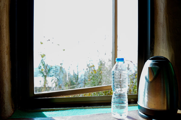 关闭的瓶子和水壶都为客人安排在酒店房间的窗户旁边。在早晨的阳光下，从地球房子窗户看到美丽的景色。泰国北部的酒店。图片下载