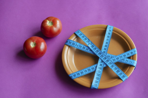 用卷尺把新鲜的西红柿放在紫色的背景和盘子上。图片下载