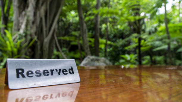 在一家以树木和森林为背景的餐厅的叠层木桌上，用不锈钢板制成的预留标志。图片下载