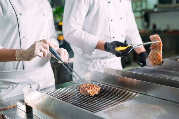 厨师们在餐馆或旅馆厨房的炉子上烤肉。图片下载