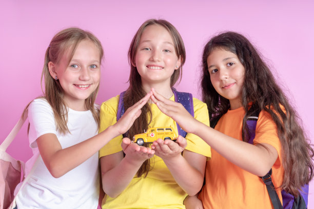 三个女生手里拿着一辆玩具校车。儿童在学校的安全概念。回到学校。工作室的照片。图片下载