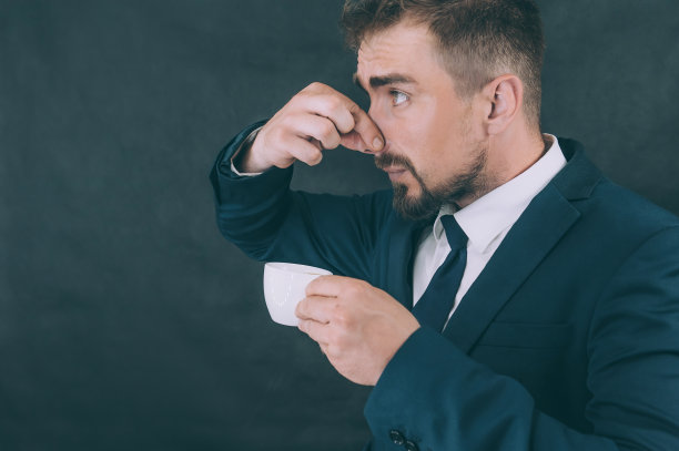 深色背景上穿着夹克的商人，手里拿着一杯咖啡。图片下载