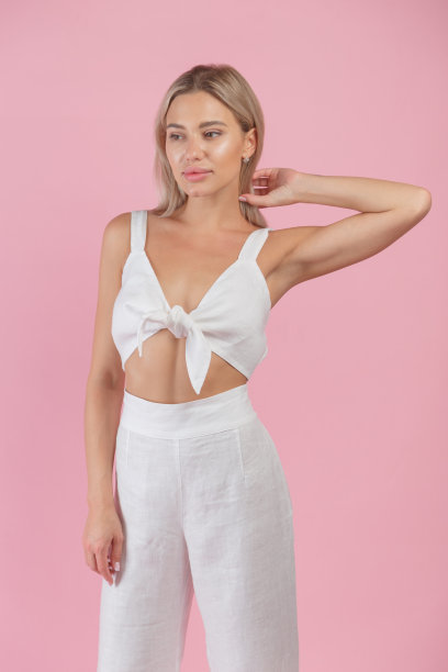 年轻的金发女人在白色自然亚麻看和绿色高跟鞋在粉红色的背景图片下载