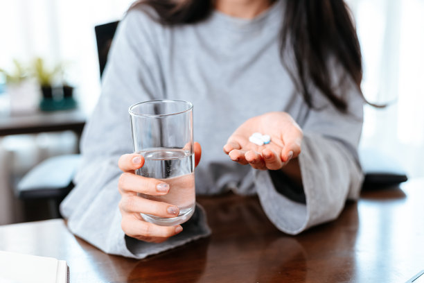 在家里工作的女商人手里拿着一杯水，手里拿着一粒白色的圆形药丸。图片下载