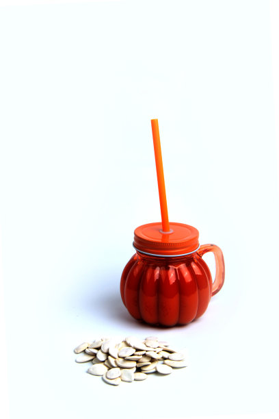 瓶南瓜汁和成堆的南瓜籽孤立在白色的背景。垂直的图像图片下载