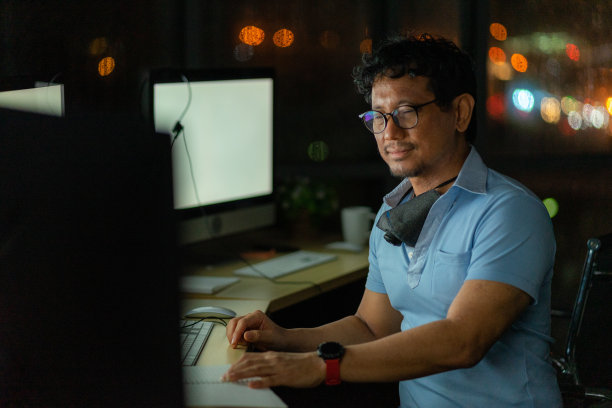 工程技术人员晚上工作或什么时候带着电脑显示器和耳机在办公室工作图片下载