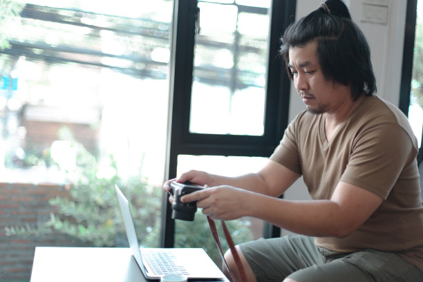 亚洲男性观看在线培训研讨会的相机功能的笔记本在客厅图片下载