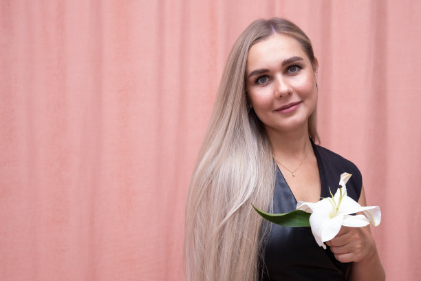 最美丽的女孩的肖像与华丽光滑的长发与她的手一朵花在粉红色的背景图片下载
