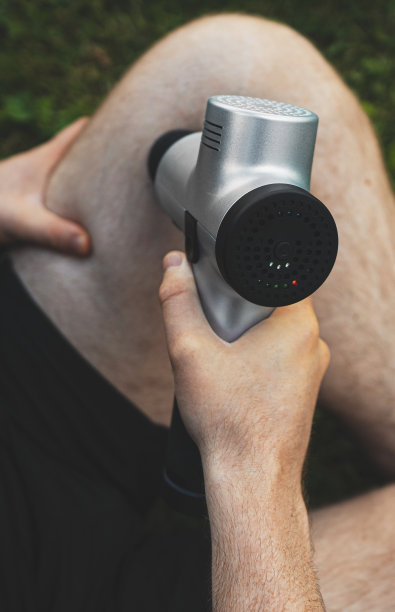 男人在锻炼后用按摩敲击器按摩腿。图片下载